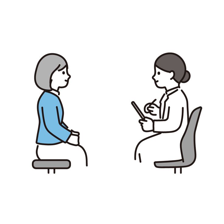 This may contain: a woman sitting on a chair talking to another woman who is looking at her phone